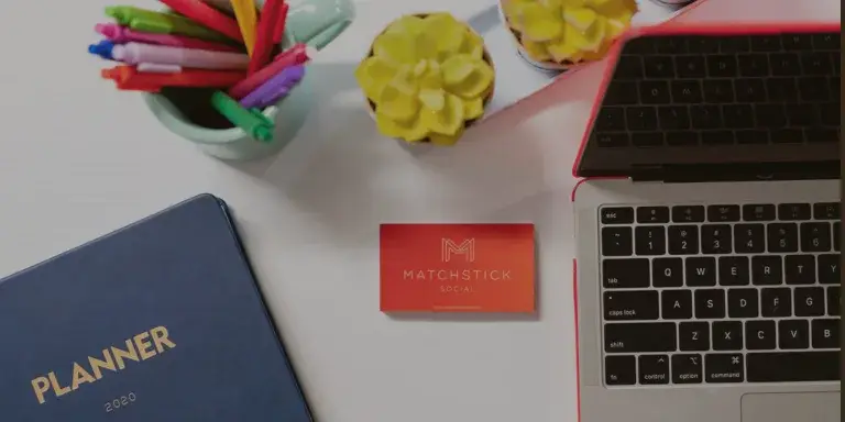 Overhead view of a clean workspace with a laptop, planner, colorful pens, small plants, and a business card reading ‘Matchstick Social,’ representing a modern, organized digital marketing setup.”